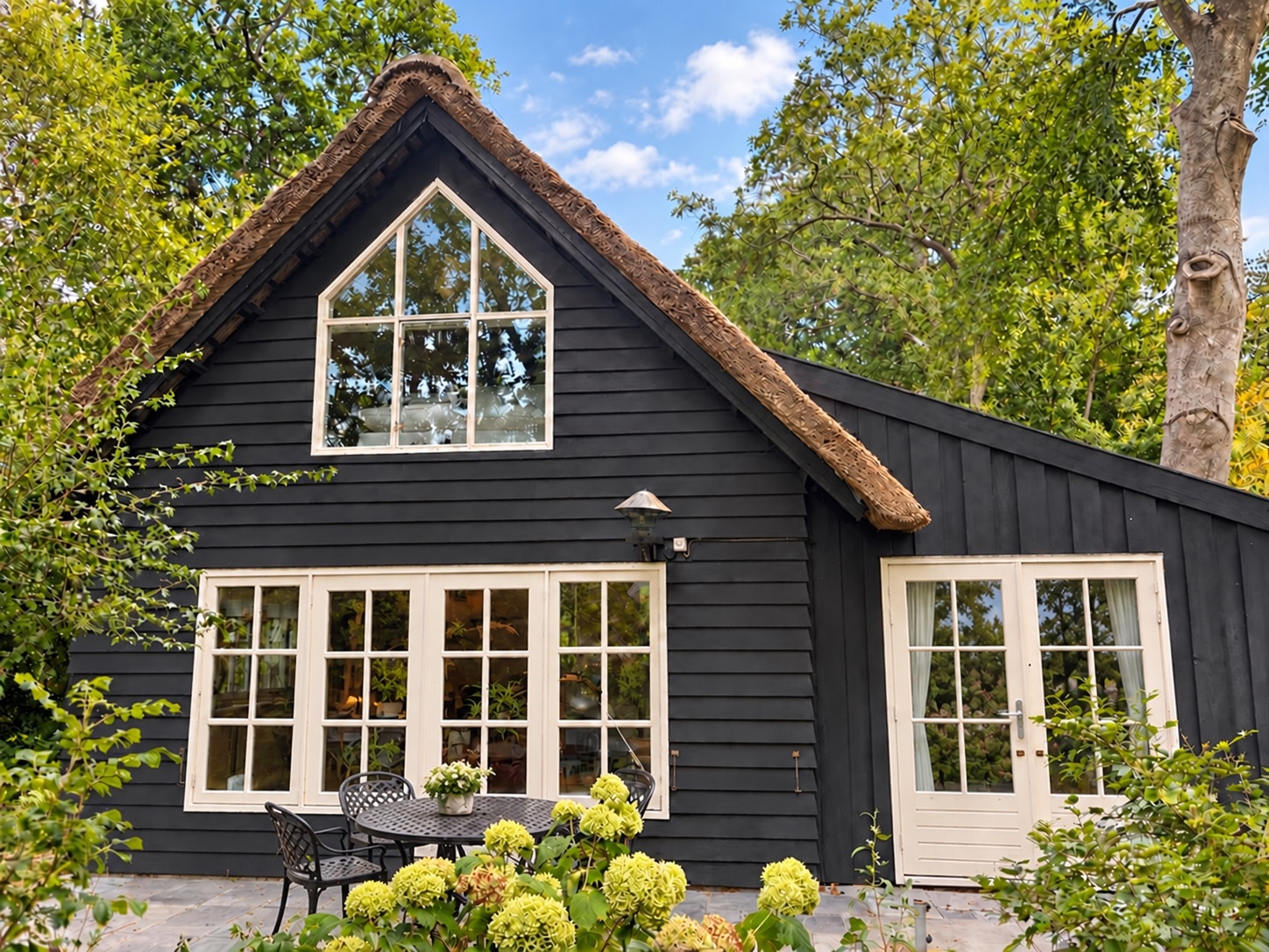 The facade with its tall studio window and thatched roof in summer greenery